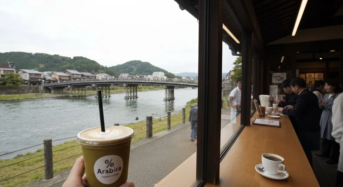 el mostrador de caja de cristal de % Arabica Arashiyama junto al río, un Kyoto Latte en mano con el puente Togetsukyo y el río Katsura al fondo